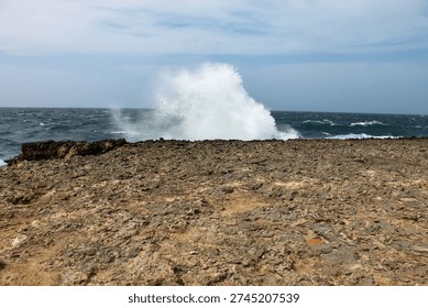 A dramatic close up of ocean waves breaking over a rocky shoreline in a Curacao nature reserve. The vibrant white sea foam forms a striking bright border against the dark volcanic stones, capturing the rhythmic movement and raw beauty of the Caribbean coast