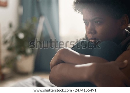Dramatic close up portrait of Black boy crying and hugging knees in hazy dark room with blurred background copy space