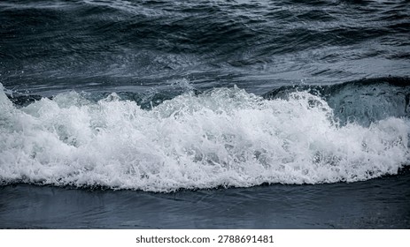 Dramatic close up of a powerful ocean wave crashing into white foam and sea spray against dark, deep blue water, capturing the raw energy of nature's power.
