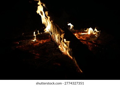 Dramatic close-up of fire flames licking a dark wooden log at night