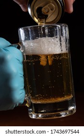 Dramatic close-up of a gloved hand holding a mug, with beer being poured from a can during quarantine. - Shutterstock ID 1743697544