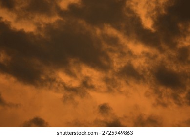 A dramatic close-up of heavy storm clouds saturated with the intense amber light of a setting sun