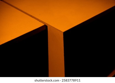 Dramatic close-up of intersecting orange surfaces, illuminated by a vibrant light leak. Abstract composition with sharp angles, contrasting textures, and a dark background.
