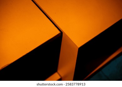 Dramatic close-up of intersecting orange surfaces, illuminated by a vibrant light leak. Abstract composition with sharp angles, contrasting textures, and a dark background.