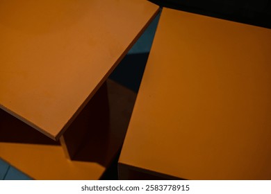 Dramatic close-up of intersecting orange surfaces, illuminated by a vibrant light leak. Abstract composition with sharp angles, contrasting textures, and a dark background.