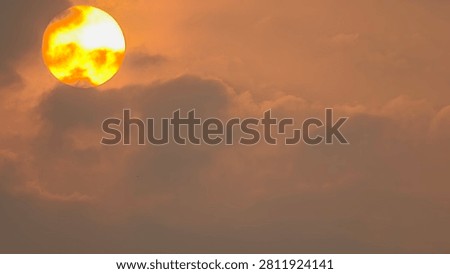Dramatic close-up of a large glowing golden sun or full moon partially hidden behind dark, moody clouds during a misty sunset or sunrise