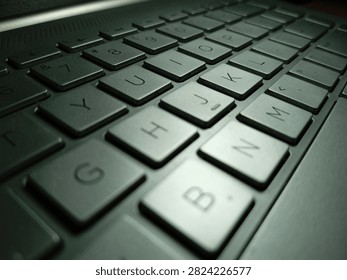 A dramatic close-up macro shot captures the angular keys of a computer keyboard from a low, dynamic perspective, showcasing the letters H, J, K, B, N, M, U, I, O, and surrounding number keys in sharp detail against a moody, low-light setting. Strategic side lighting creates striking contrast across the beveled, slightly worn key surfaces, highlighting subtle texture and wear patterns from regular use, while deep shadows fall between each key, emphasizing their three-dimensional square-cut design