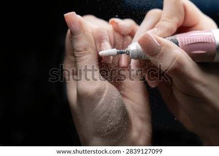 Dramatic close-up of professional manicure using pink electric nail drill creating fine dust on client’s nails against dark background. Ideal for beauty, cosmetics, nail salon and wellness marketing