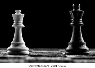 A dramatic close-up shot of black and white chess king pieces positioned opposite each other on a chessboard, set against a dark background.