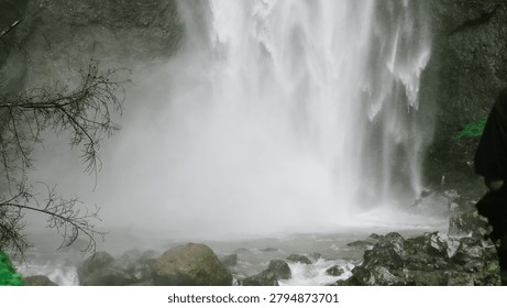A dramatic close-up view of a powerful tropical waterfall cascading over rugged cliffs into a rocky river below. The misty atmosphere and natural surroundings create a breathtaking landscape, making this image perfect for travel, eco-tourism, environmental conservation, and nature-themed projects.