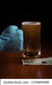 Dramatic close-ups of gloved hands of a bartender or patron at a bar or restaurant, during quarantine, handling a glass/mug of beer with money against a wooden bar top with a black background.  - Shutterstock ID 1743694400