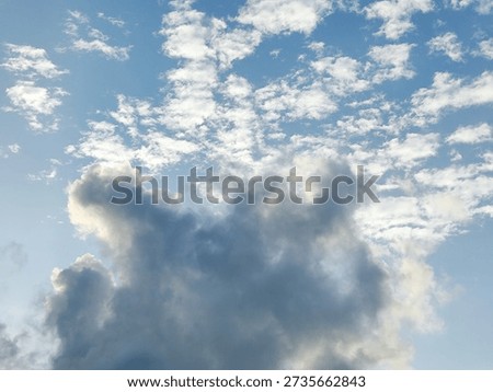 Dramatic cloud formation rising upward with textured white clouds spread across a bright blue sky.