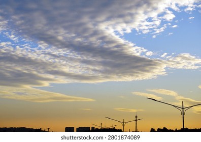 Dramatic cloud formations over a city skyline at sunset, with silhouetted streetlights and a warm evening glow creating a calm urban atmosphere.