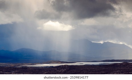 Dramatic cloud-covered landscape with sunlight filtering through over a serene lake.