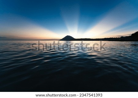 Dramatic cloudless sunset with sunbeams behind the volcano island at Bunaken, Sulawesi, Indonesia