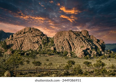 Dramatic clouds color the sky as the sunset casts a warm glow over an impressive formation of rocky hills