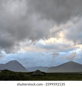 Dramatic clouds dominate, hinting at light above distant peaks. A lone boulder sits in a green valley, framed by rolling hills. Moody, atmospheric Scottish landscape.