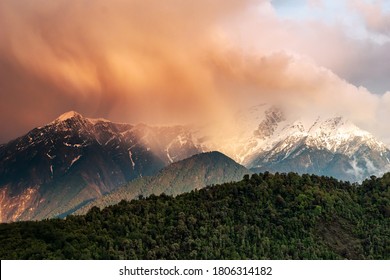Dramatic clouds drenched in red and orange sunset colours showering rain on the snow capped mountains in the Himalayan village of Munsyari in the state of Uttarakhand in India.