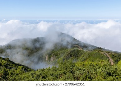 Dramatic clouds enveloping lush green hills in Madeira, Portugal. Misty mountain landscape with dense forest. Ocean view under a bright sky. Natural scenic beauty of the island.