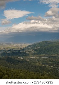 Dramatic clouds hover over a green mountain valley and farmland near Chilliwack, British Columbia, Canada.