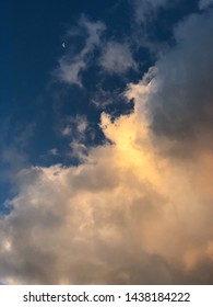 Dramatic clouds illuminated by orange sunlight during sunrise with moon against dark blue skies