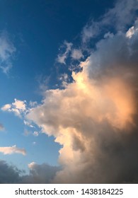 Dramatic clouds illuminated by orange sunlight during sunrise with moon against dark blue skies