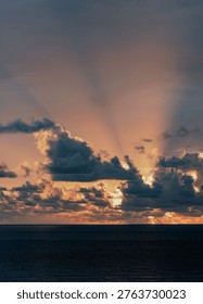 Dramatic clouds are illuminated by the soft glow of a setting sun, showcasing nature's artistry in this captivating display of light and form over the ocean horizon.