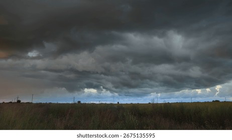 Dramatic clouds loom over open field in rural landscape. Dark, stormy atmosphere creates an ominous mood during daytime.