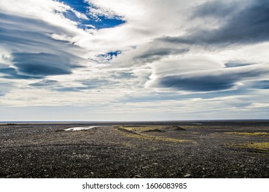 Dramatic clouds over endless volcanic beach in Icelandic landscape.