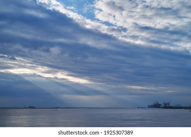 dramatic clouds over the river Weser (Germany) with silhouettes of the artificial islands Langlütjen I and II and the cranes of the seaport Bremerhaven - scenic sunrays come out of the sky