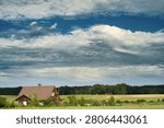 Dramatic clouds over rural countryside with farmhouse and summer fields