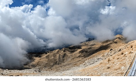 Dramatic clouds rolling over rugged mountain peaks with rocky slopes in sunlight, creating a powerful contrast of earth and sky in a breathtaking alpine view. - Powered by Shutterstock - Get 15% off with code: PIKWIZARD15