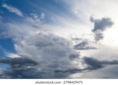 Dramatic clouds swirl above a bright blue sky. Sunlight breaks through, casting soft glow. Darkening masses hint at an approaching storm. Ideal for weather scenes or nature photography
