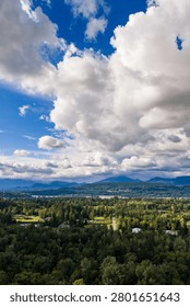 Dramatic cloudscape and blue sky above a verdant Fraser Valley landscape in BC, Canada with distant mountains.