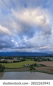 Dramatic cloudscape and stormy sky above Fraser Valley farmland near Chilliwack, British Columbia, Canada, with river and distant mountains.