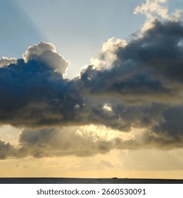 Dramatic cloudscape with sunbeams piercing through dark storm clouds over a calm ocean.