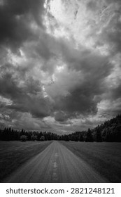Dramatic cloudscape, sunrays, straight dirt road in the forest meadow, black and white photo