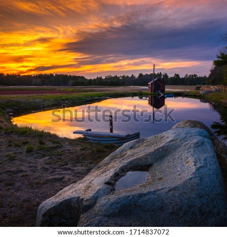 Dramatic cloudscape at sunset and reflections on pump house pond and boulder