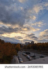 Dramatic cloudy evening sky over a city street with autumn trees and tall buildings in the distance