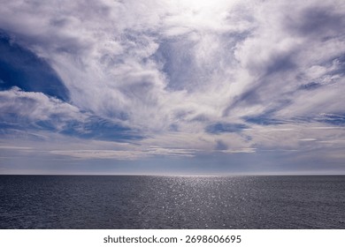 Dramatic cloudy sky above calm shimmering sea at horizon line.