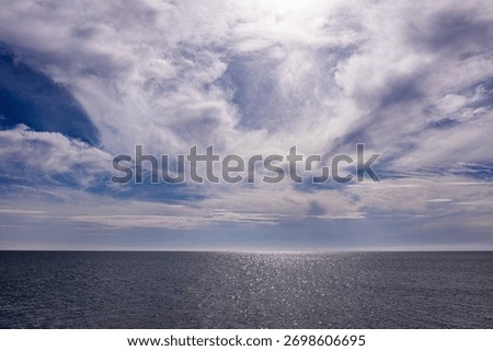 Dramatic cloudy sky above calm shimmering sea at horizon line.