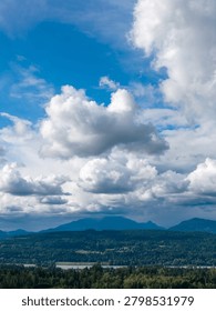 Dramatic cloudy sky above Fraser Valley mountains with lush forest, river and blue horizon in BC, Canada.