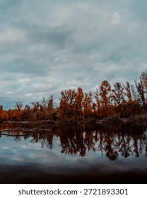 Dramatic cloudy sky above orange treeline and reflections