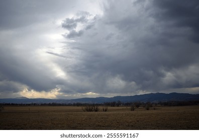 A dramatic cloudy sky casting shadows over expansive open fields with distant mountain views.