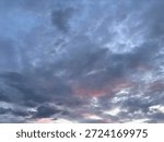 Dramatic cloudy sky during dusk with layered dark clouds and subtle pink sunset light. Atmospheric evening sky background for weather, nature, emotional mood, and abstract concepts.