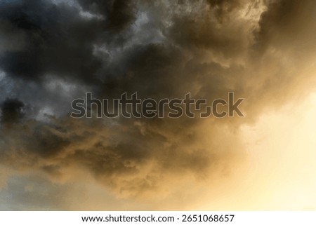 Dramatic cloudy sky with golden sunlight breaking through dark storm clouds during sunset, creating a moody atmospheric scene in nature.