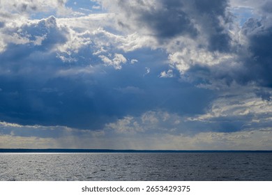 Dramatic cloudy sky over a calm sea horizon, natural light breaking through heavy clouds over the ocean, atmospheric weather landscape with dark storm clouds and rays of sun shining through