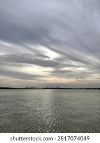 Dramatic cloudy sky over calm sea waters with distant city skyline on the horizon at sunset.