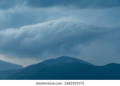 Dramatic cloudy sky over dark mountain range creating a moody and serene natural landscape scene