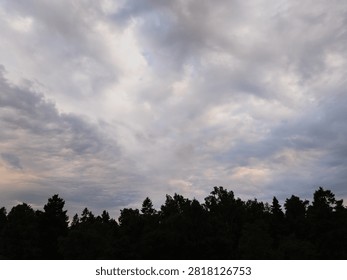 Dramatic cloudy sky over dark forest silhouetted treetops during evening twilight captured from drone in natural landscape of Estonia. 